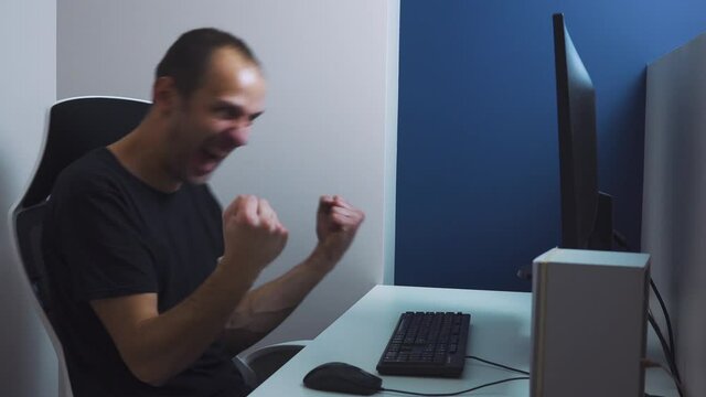 Excited funny businessman shouting of joy and gesturing with raised clenched fists over successful business deal in front of a computer over dark.