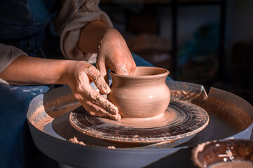 Close-up A woman potter in beautifully sculpts a deep bowl of brown clay and cuts off excess clay on a potter's wheel in a beautiful workshop