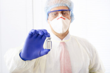 Naklejka premium Middle aged male health care worker in cap gloves and scrub with vial glass of liquid medicine