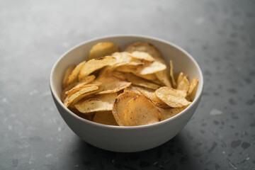 Organic potato chips with black pepper in white ceramic bowl on concrete background
