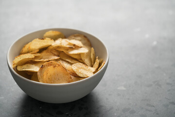 Organic potato chips with black pepper in white ceramic bowl on concrete background with copy space