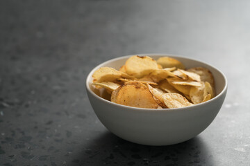 Organic potato chips with black pepper in white ceramic bowl on concrete background with copy space