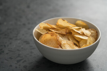 Organic potato chips with black pepper in white ceramic bowl on concrete background with copy space