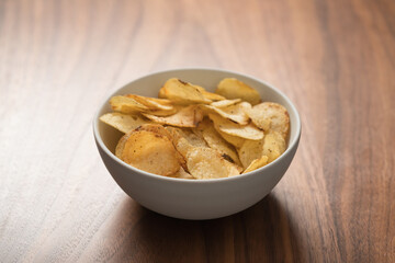 Organic potato chips with black pepper in white ceramic bowl on walnut wood background with copy space