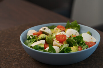 Salad with avocado, cherry tomatoes, romaine and mozzarella in blue bowl on walnut table with copy space