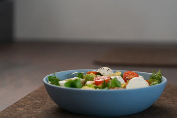 Salad with avocado, cherry tomatoes, romaine and mozzarella in blue bowl on walnut table with copy space