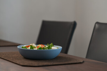 Salad with avocado, cherry tomatoes, romaine and mozzarella in blue bowl on walnut table with copy space