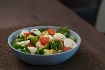 Salad with avocado, cherry tomatoes, romaine and mozzarella in blue bowl on walnut table with copy space