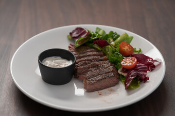 ribeye steak with garlic sauce and fresh salad on white plate on walnut table