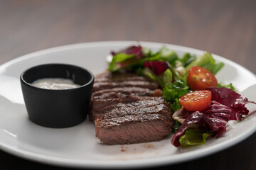 ribeye steak with garlic sauce and fresh salad on white plate on walnut table