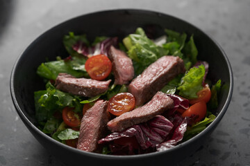 Steak salad with cherry tomatoes and mixed greens in black bowl
