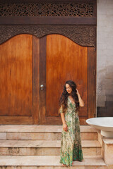 Portrait of brunette curly woman in green silk dress on background of wooden door. Asian style and architecture.