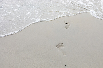 Sea water coming on the white beach sand with footprint