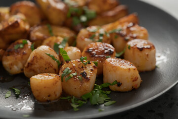 roasted scallops with baked potatoes wedges on a black plate