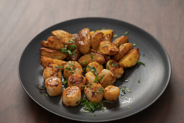 roasted scallops with baked potatoes wedges on a black plate on walnut wood background