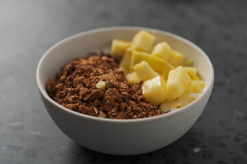 chocolate granola with mango and greek yogurt in white bowl on concrete background