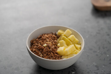 chocolate granola with mango and greek yogurt in white bowl on concrete background