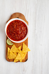 Homemade Tomato Salsa and Nachos on a rustic wooden board on a white wooden surface, overhead view. Flat lay, top view, from above. Copy space.