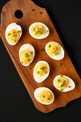 Homemade Deviled Eggs with Chives on a rustic wooden board on a black surface, top view. Flat lay, overhead, from above.