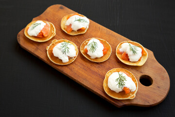 Homemade Blini with Smoked Salmon, Creme and Dill on a rustic wooden board on a black background, side view.