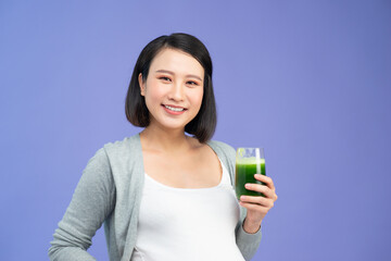 A beautiful woman in her late pregnancy is taking care of herself and her child by drinking a green smoothie.