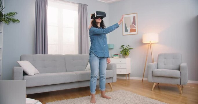 Beautiful adult woman looking at pictures in virtual reality while being at home. Pretty Caucasian lady swiping and zooming photos with hand in air indoors. Technology, furute, entertainment concept.