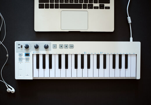 The musician's workplace. MIDI keyboard, laptop and wired headphones on a black background. Flat lay.