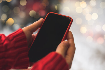 Cropped of woman's hands in red sweater holding smartphone with blank screen of gadget at Christmas...