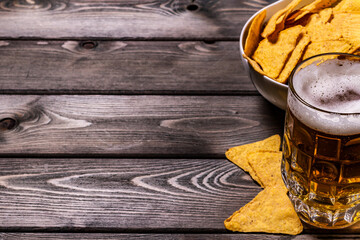 A mug of cold frothy beer with nachos corn chips on a wooden background. top view.