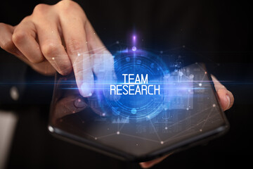 Young man holding a foldable smartphone with TEAM RESEARCH inscription, educational concept
