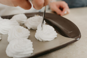 А close photo of the hands of a woman who is creating with a spoon a form of meringues on a tray. A girl is preparing to cook a delicious lemon meringue tart.