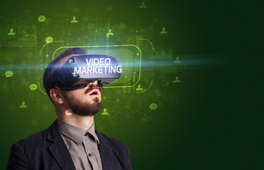 Businessman looking through Virtual Reality glasses with VIDEO MARKETING inscription, social networking concept