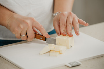Fototapeta na wymiar А close photo of the hands of a young woman who is cutting fresh butter on a cutting board with a sharp knife.