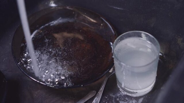Tap water is poured into plate. Black dink in kitchen with dirty dishes.