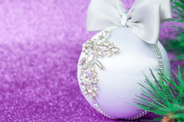 White Christmas ball in rhinestones for Christmas tree decoration. Christmas toy. Christmas toy for decorating a Christmas tree on a lilac background. Shining crystals on a white ball.