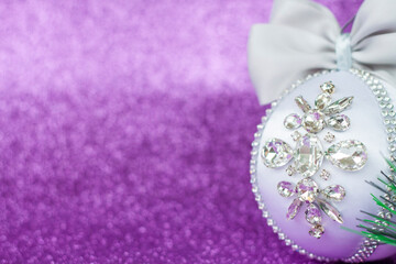 Obraz na płótnie Canvas White Christmas ball in rhinestones for Christmas tree decoration. Christmas toy. Christmas toy for decorating a Christmas tree on a lilac background. Shining crystals on a white ball.