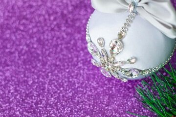 White Christmas ball in rhinestones for Christmas tree decoration. Christmas toy. Christmas toy for decorating a Christmas tree on a lilac background. Shining crystals on a white ball.