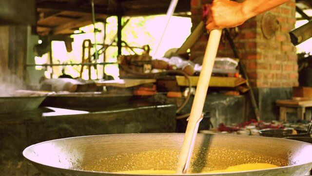 Coconut sugar production process. Farmer stir evaporated coconut sap in the wok and lift up to check the concentration.