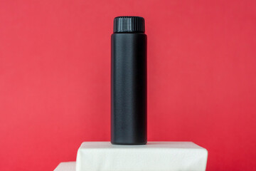Black bottles of cream stand on white multi-level stands. Black bottles on a red background. Skin care, Moisturizing and nourishing or sunscreen.