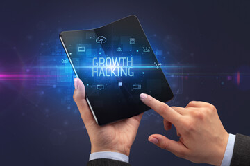 Businessman holding a foldable smartphone with GROWTH HACKING inscription, cyber security concept