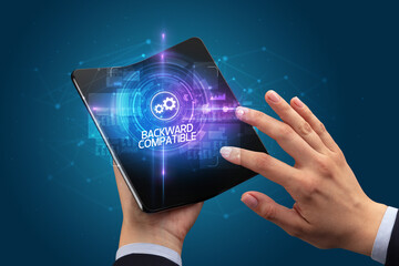 Businessman holding a foldable smartphone with COMPUTING inscription, new technology concept BACKWARD COMPATIBLE
