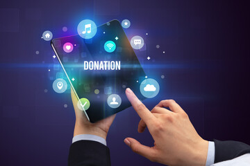 Businessman holding a foldable smartphone with DONATION inscription, social media concept