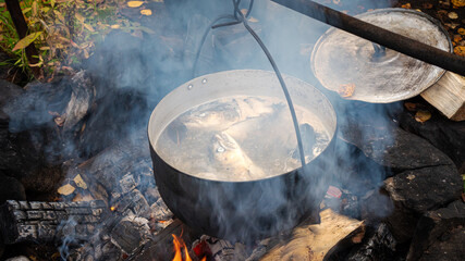 Cooking fish soup over an open fire in a kettle. Camping kitchen.