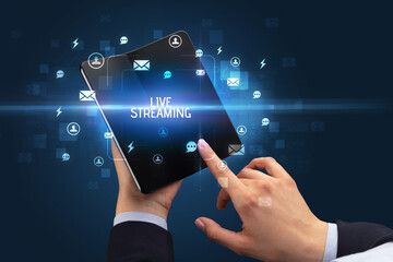 Businessman holding a foldable smartphone with LIVE STREAMING inscription, social networking concept