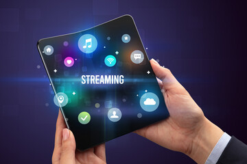 Businessman holding a foldable smartphone with STREAMING inscription, social media concept