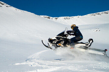 A man drives a snowmobile in the mountains. A lot of snow, blue winter sky and the rays of the sun. Kola Peninsula.