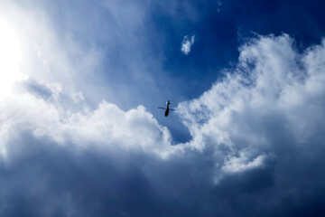 Blue sky with small helicopter flying into a thundercloud.