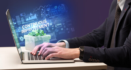 Businessman working on laptop with CONTINUOUS IMPROVEMENT inscription, cyber technology concept