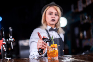 Focused woman barman makes a show creating a cocktail while standing near the bar counter in pub