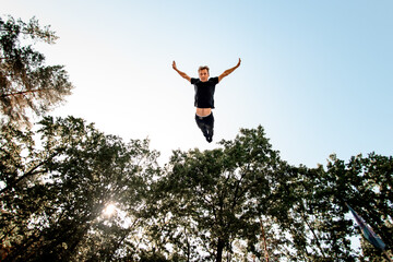 Bottom view of man in the air against blue sky and green trees.